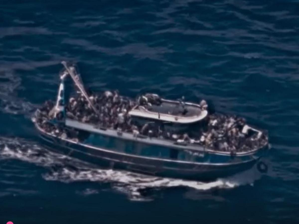 A grainy surveillance picture of an rusty boat overloaded with people