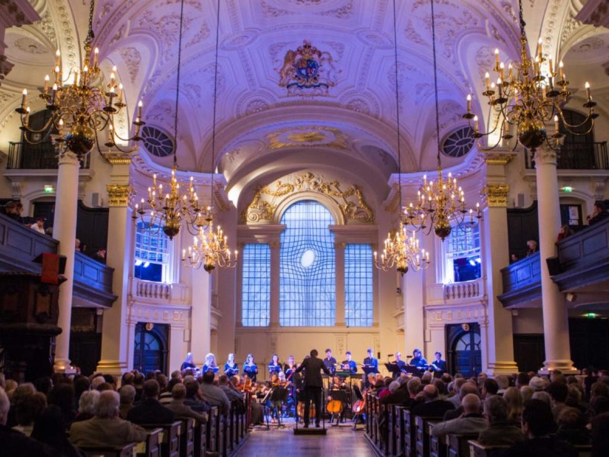 A choir sing at the front of a church while an audience looks on.