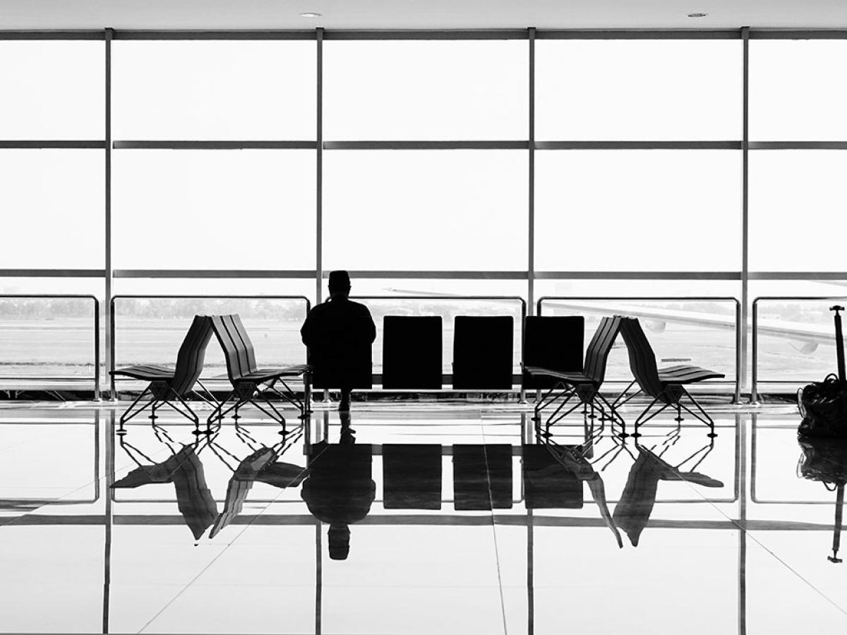 A large airport window silhouettes a bench at which one person sits.