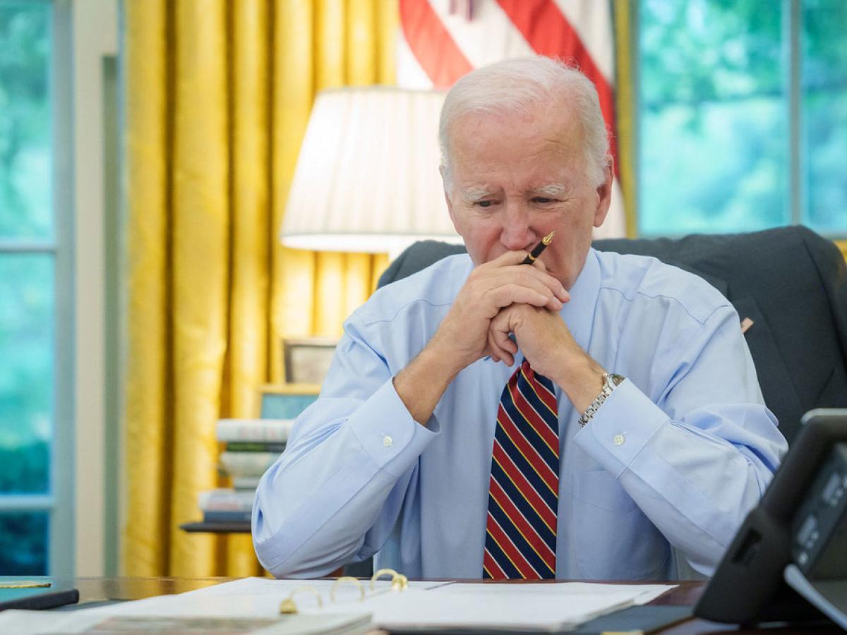 President Biden sits at a desk, holding his balled hands to his mouth.