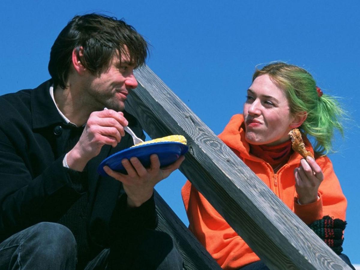 A coupe sit on outdoor steps against a blue sky. One holds a plate and the other looks towards them.