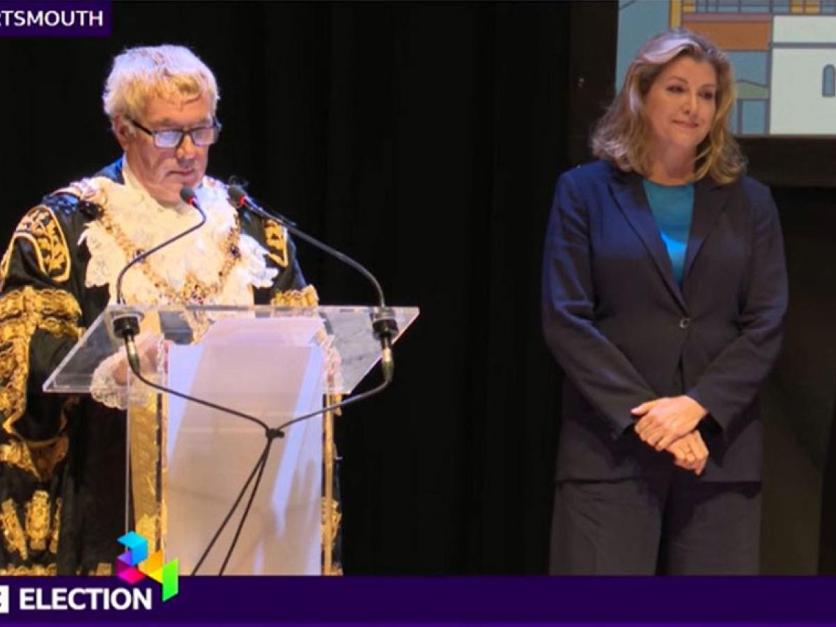 A mayor reads an election result as a despondent candidate looks on.