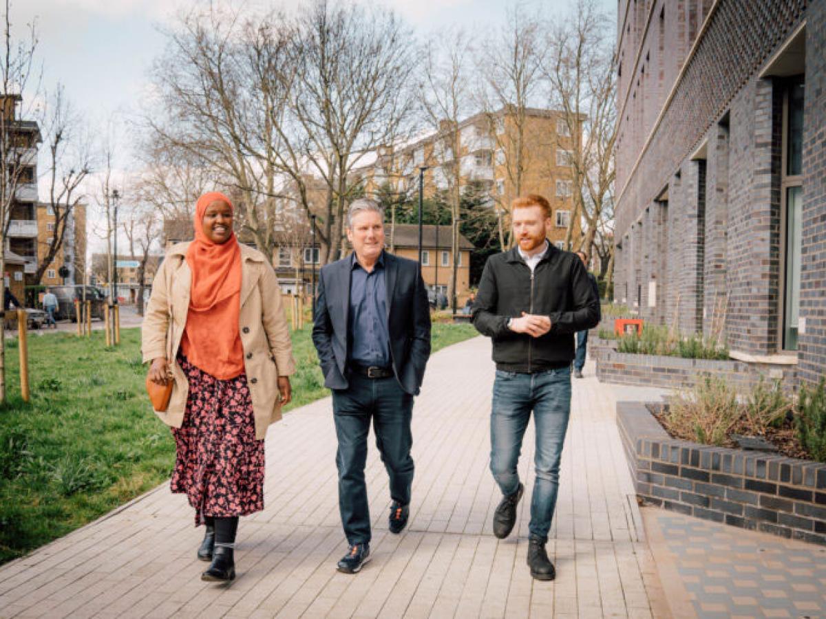 Kier Starmer walks along a residential development's path with two other people.