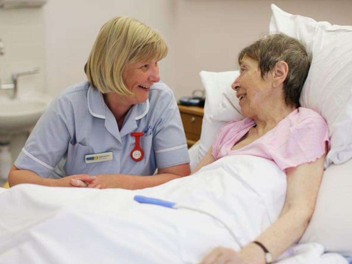 A nurse bends beside a bed and talks to a patient