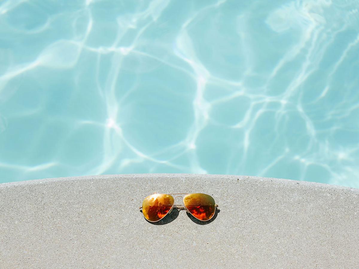 A pair of sunglasses beside a swimming pool.