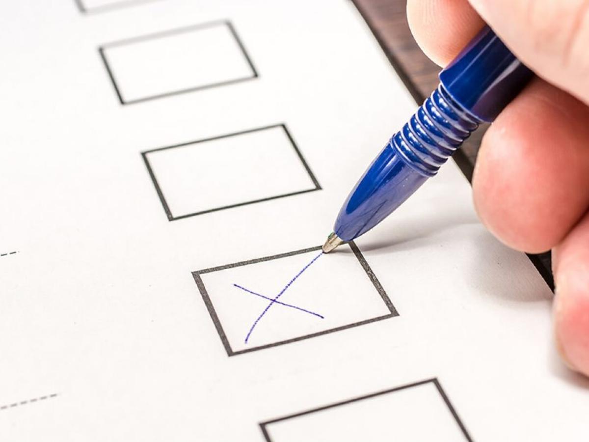 A pen draws a cross in a box on a ballot form.