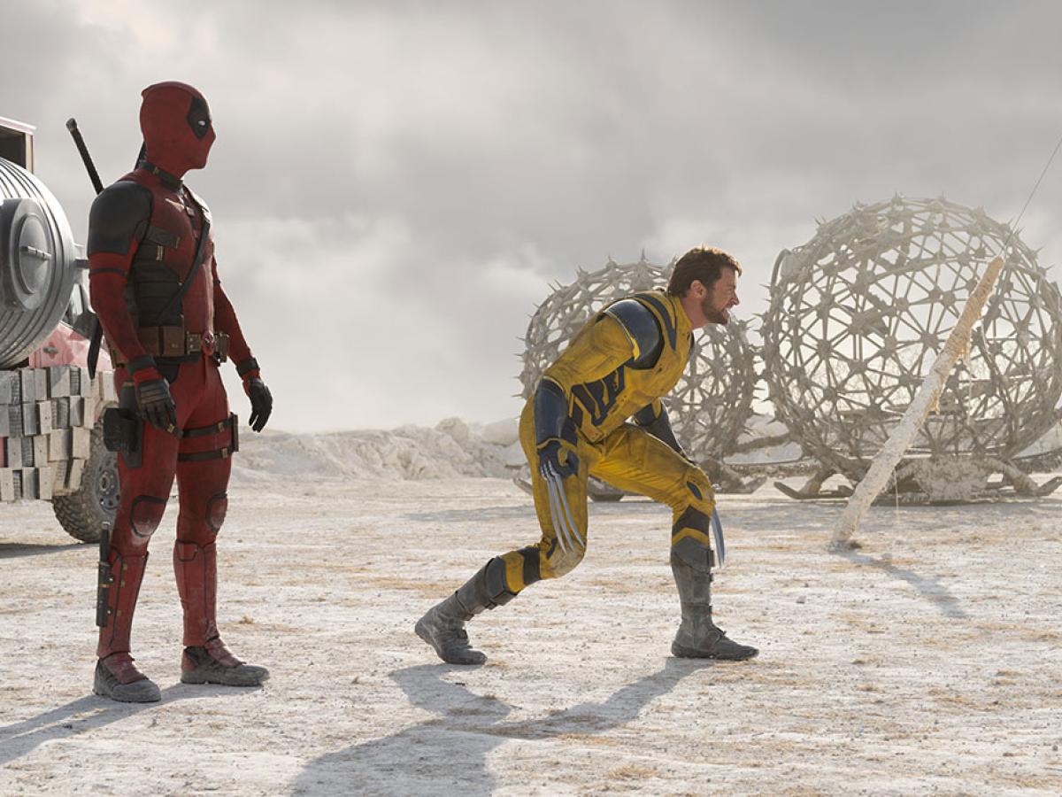 Two superheroes, deadpool and Wolverine, stand and crouch respectively, in a desert like place.