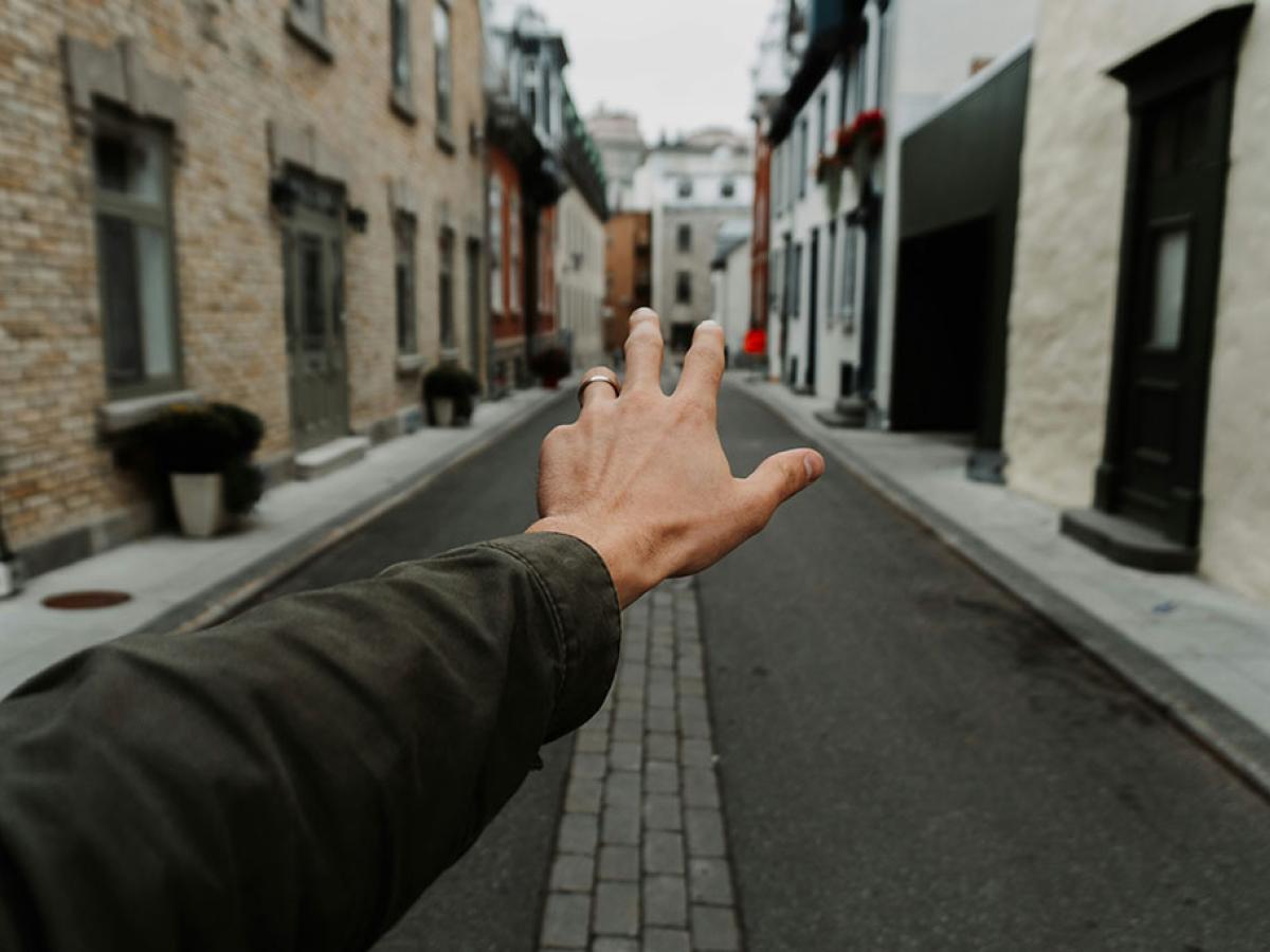 An arm and hand stretch out in front of some, a narrow street is the background.