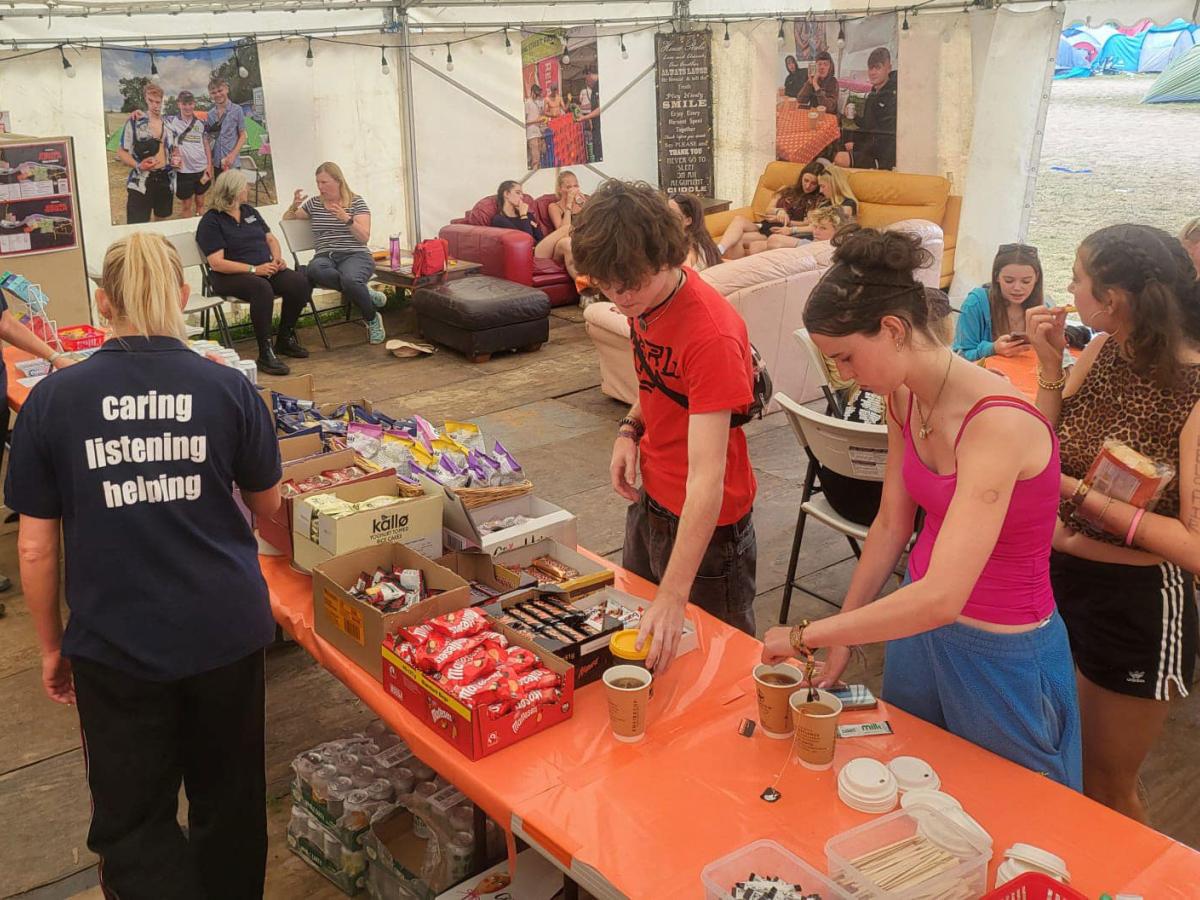 Festival goers, in a cafe tent, make drinks or sit around talking