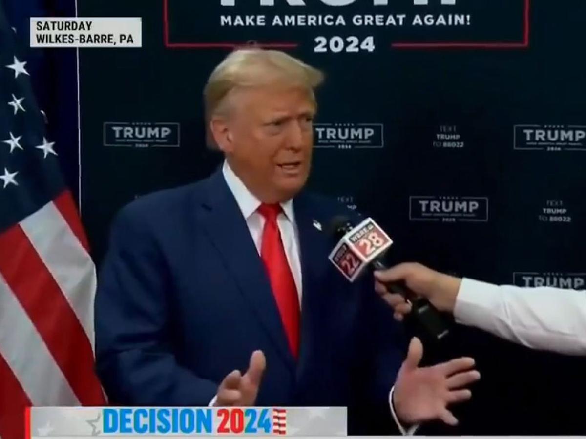 Donald Trump gestures with his hands while someone holds a mic in front of him,