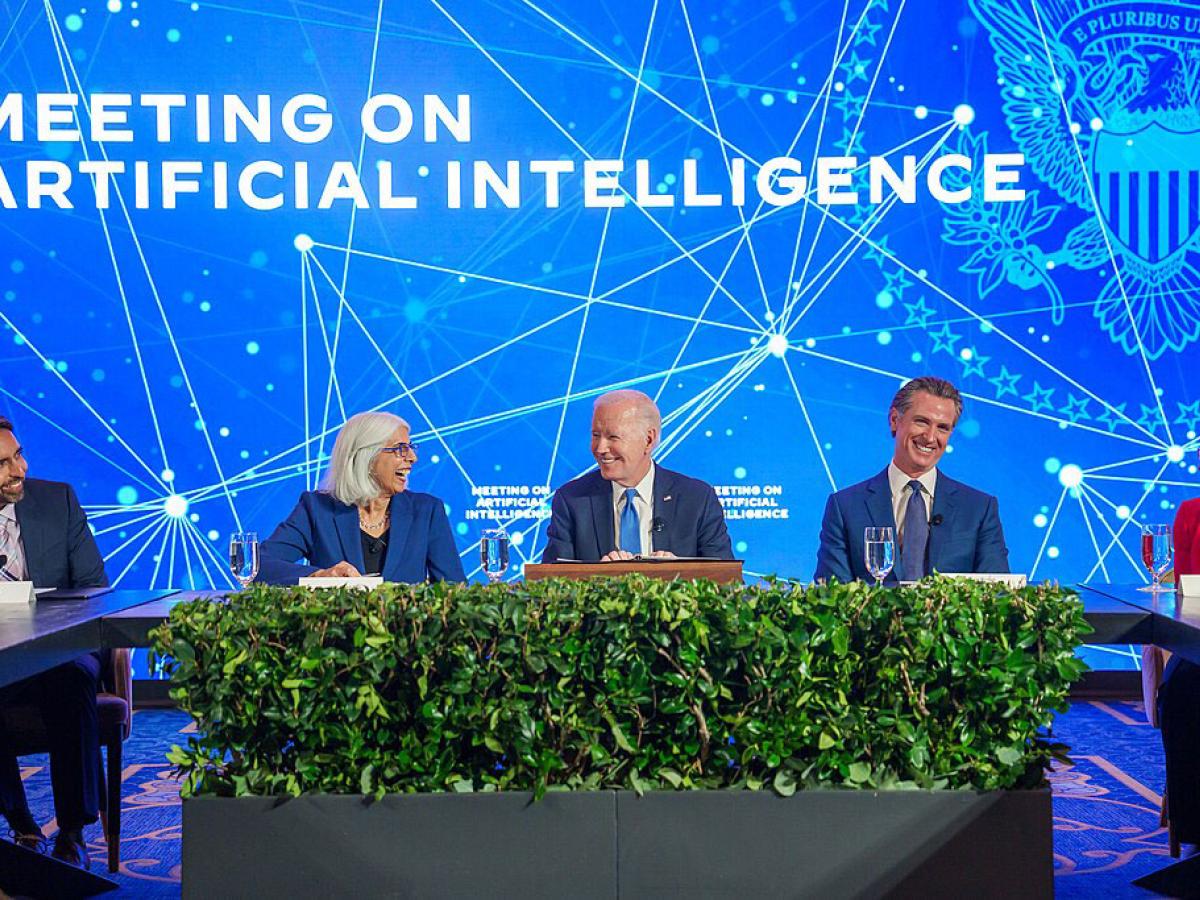 A board of experts sit at a table against a conference backdrop.