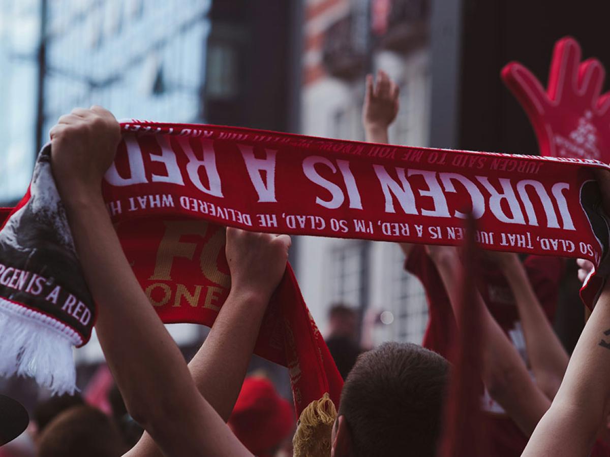 A fan holds an upside down football scrarf that reads 'Juergen is a red'.