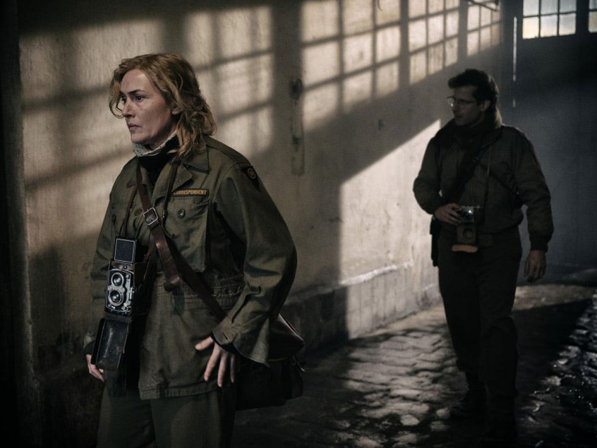 Two war photographers creep along a shadowy corridor.