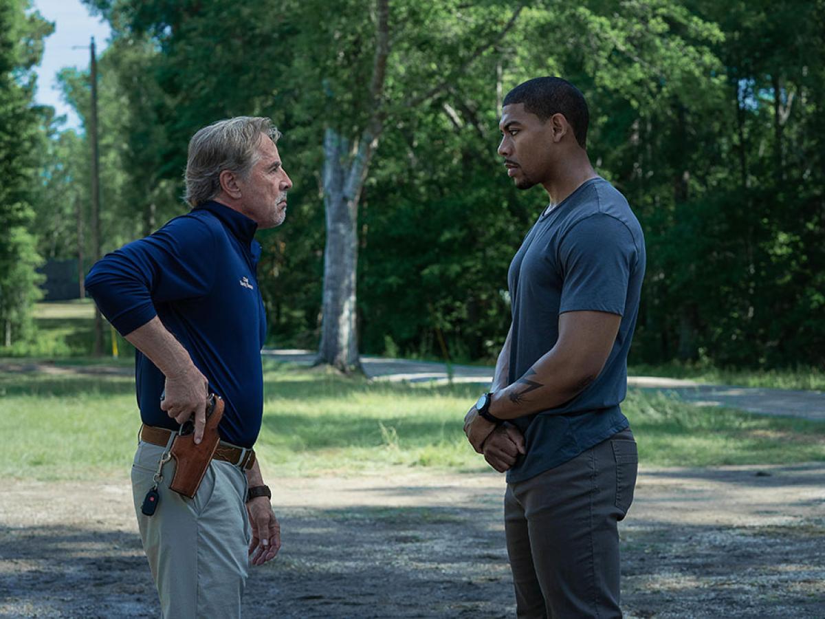 Two men stand off against each other, one holds a holstered gun.