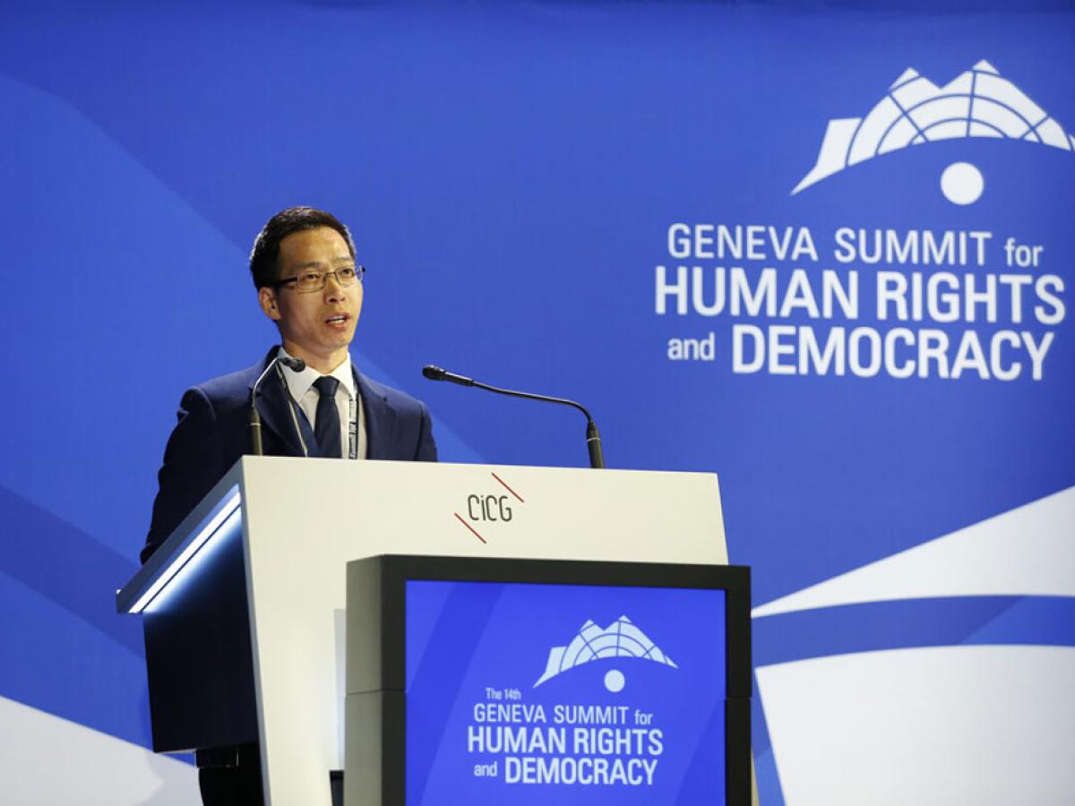 A conference speaker at a podium against a backdrop of blue.