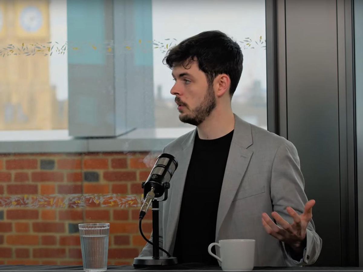 A podcast guest speaks in front of a mic and raises their hand to gesture.