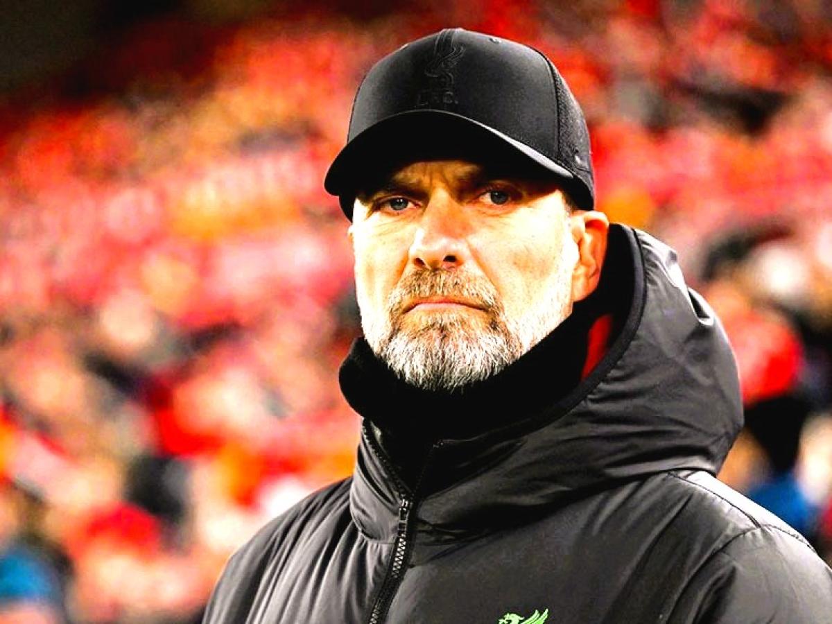 A stern looking  football manager stares hard, with a stand of supporters behind him.