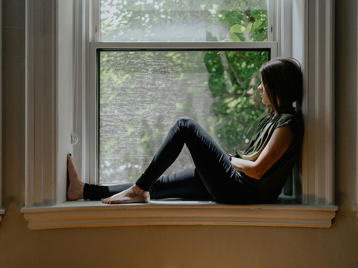 A person sits on a window sill with one raise knee.