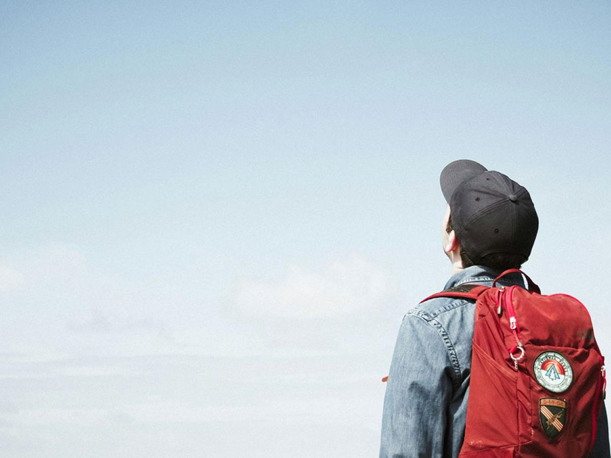 A person wearing a backpack looks to the sky.