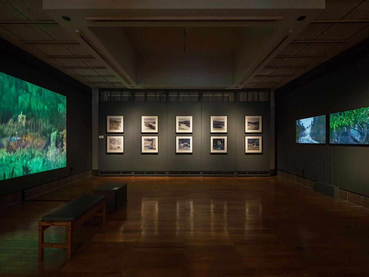 A darkened art gallery displays images and screens on three walls.