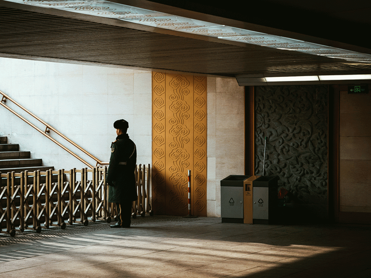 A guard stands behind a barrier across an entrance to a station escalator.