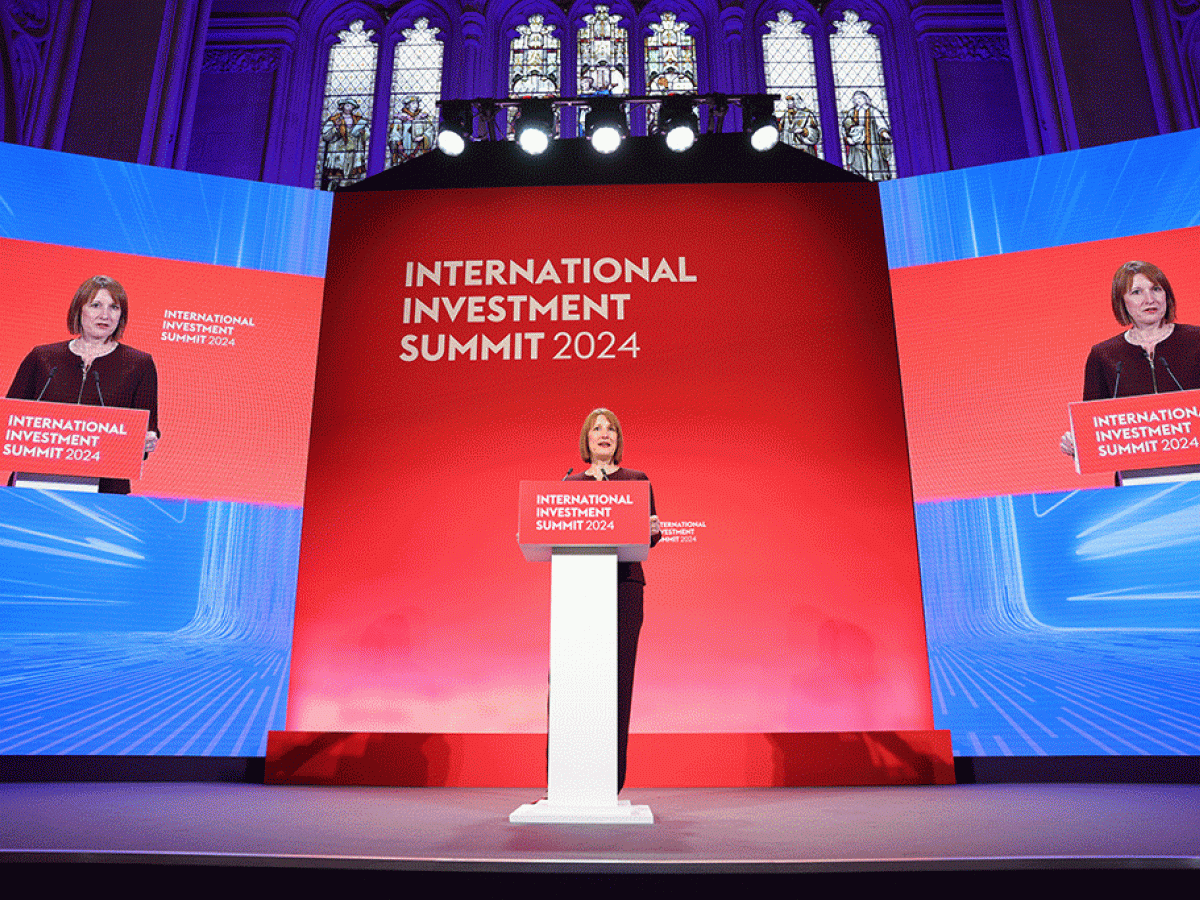 A woman stands behind a lectern against a blue and red backdrop.