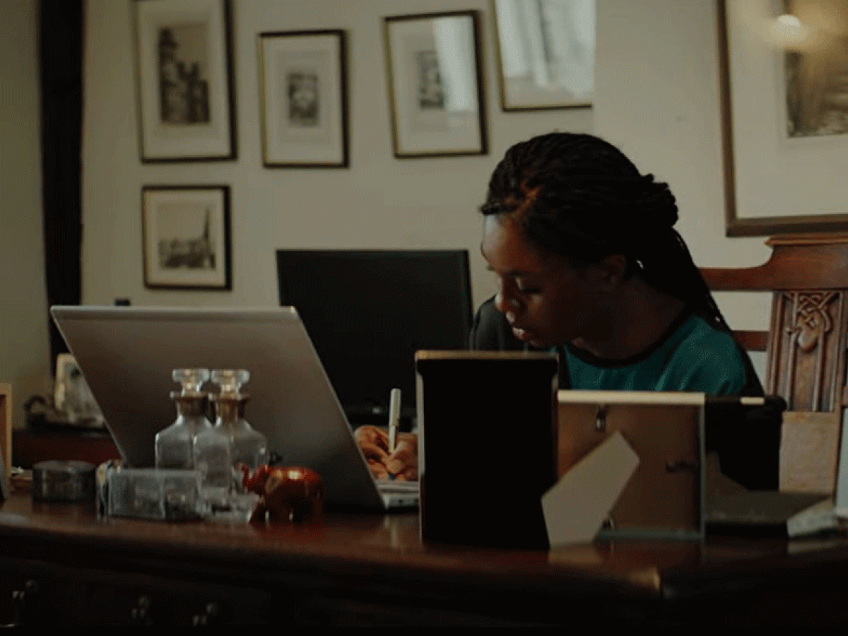 A woman works at a laptop on a desk surrounded by picture frame.