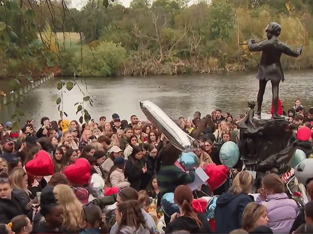 A crowd of teenagers gather by a Peter Pan statue to mourn a dead pop star