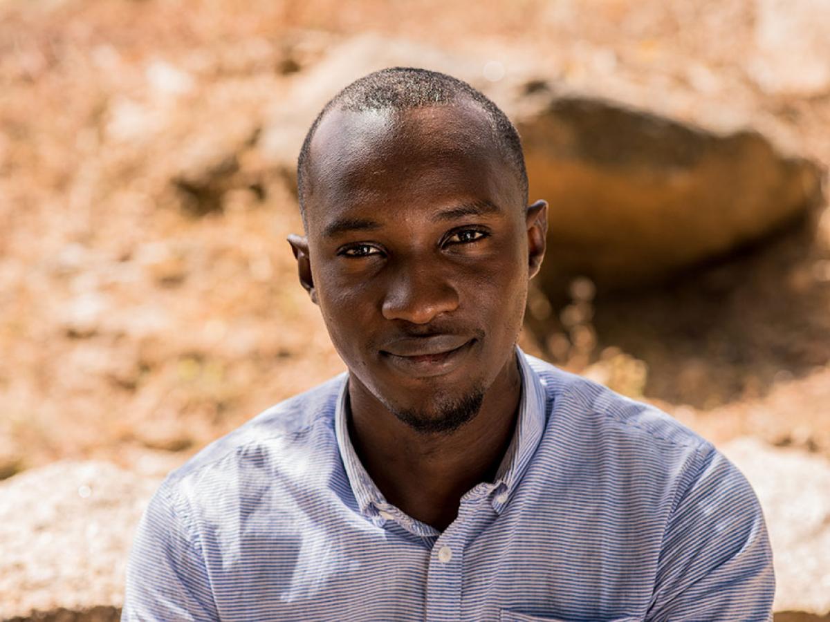 A Nigerian man looks up towards the camera, behind him is dusty ground