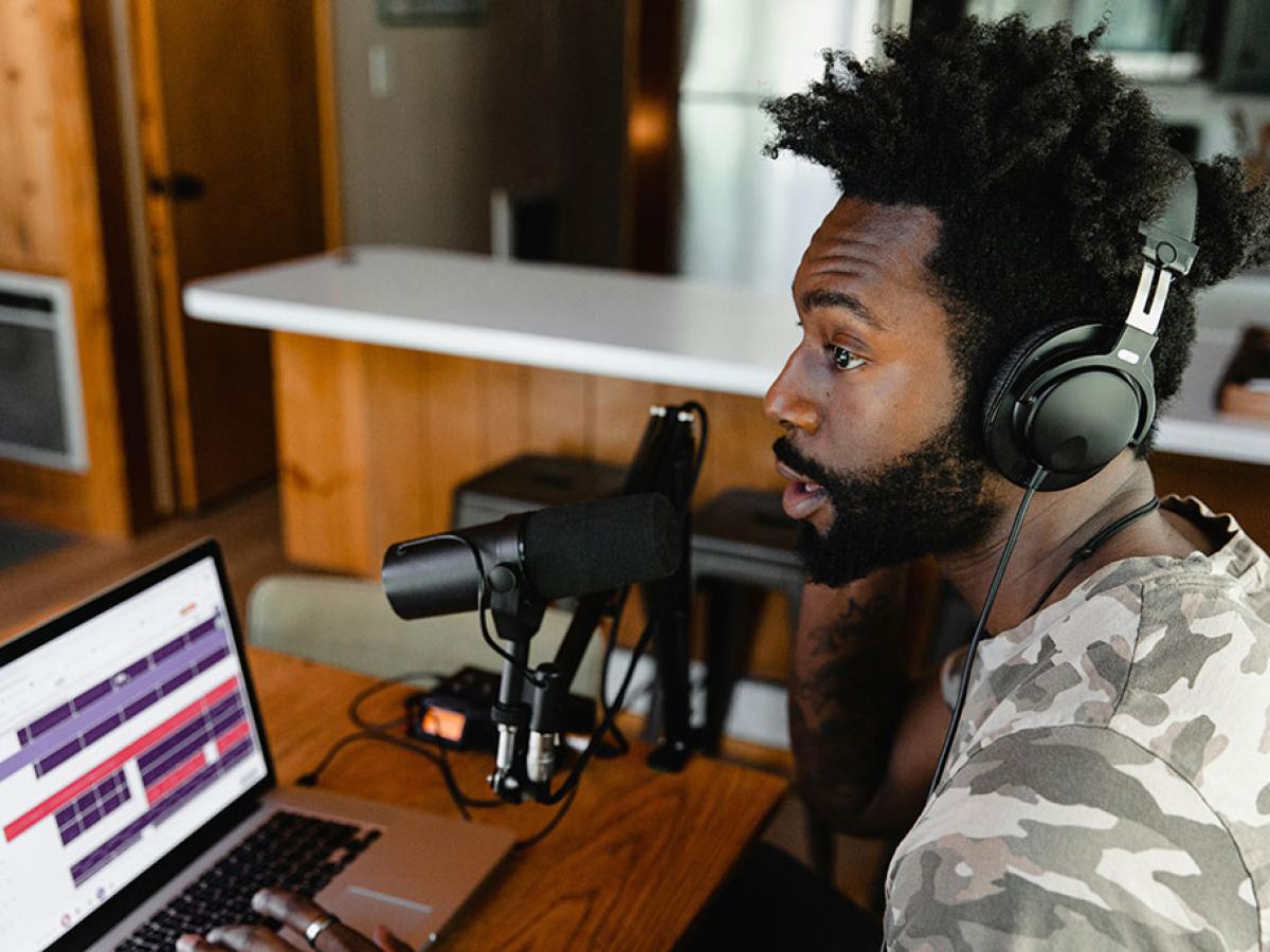 A podcaster speaks into a mic before a screen.