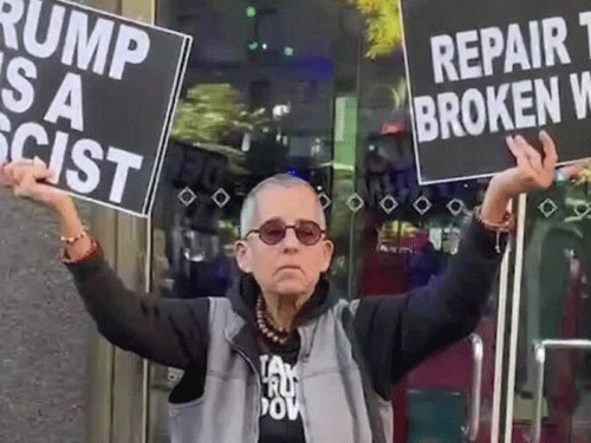 A protester holds placards up in both hands. One reads: Trump is a fascist. The other: Repair the broken world 