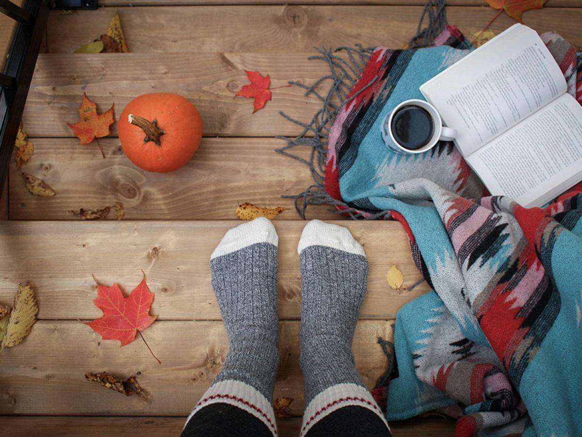 A set of be-socked feat rest on a leaf strewn step beside a book and a cup of coffee.