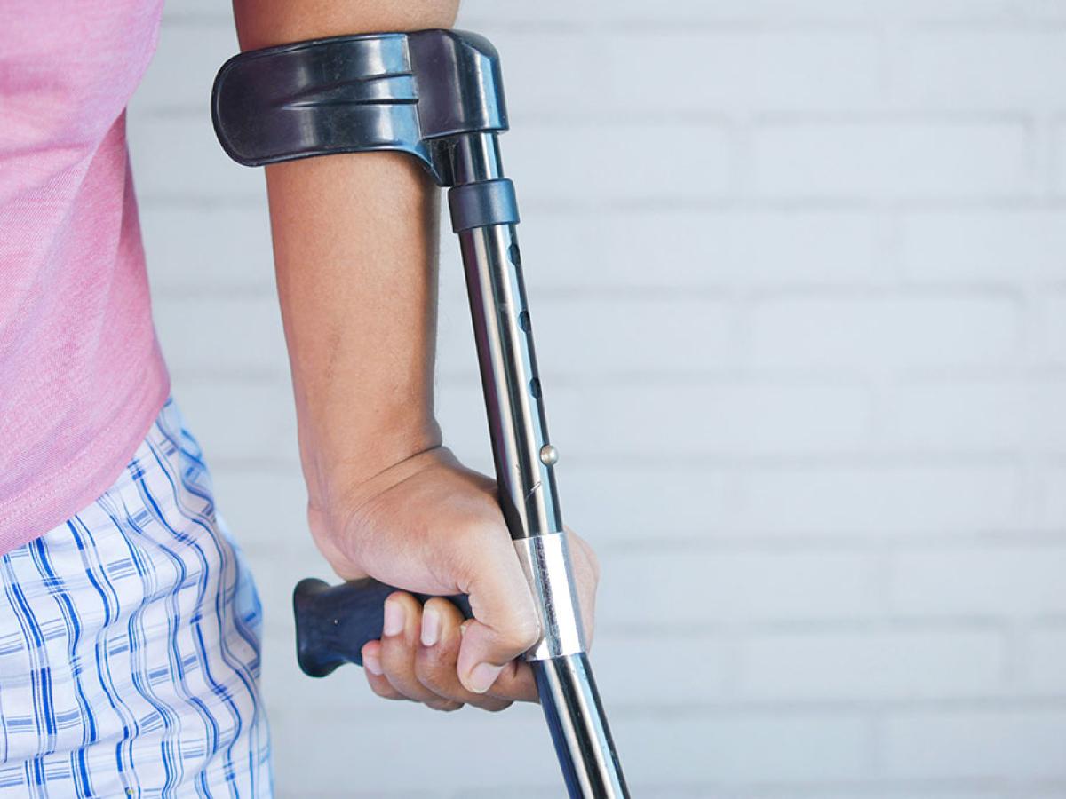 A crutch is held in the hand of someone in pyjamas.