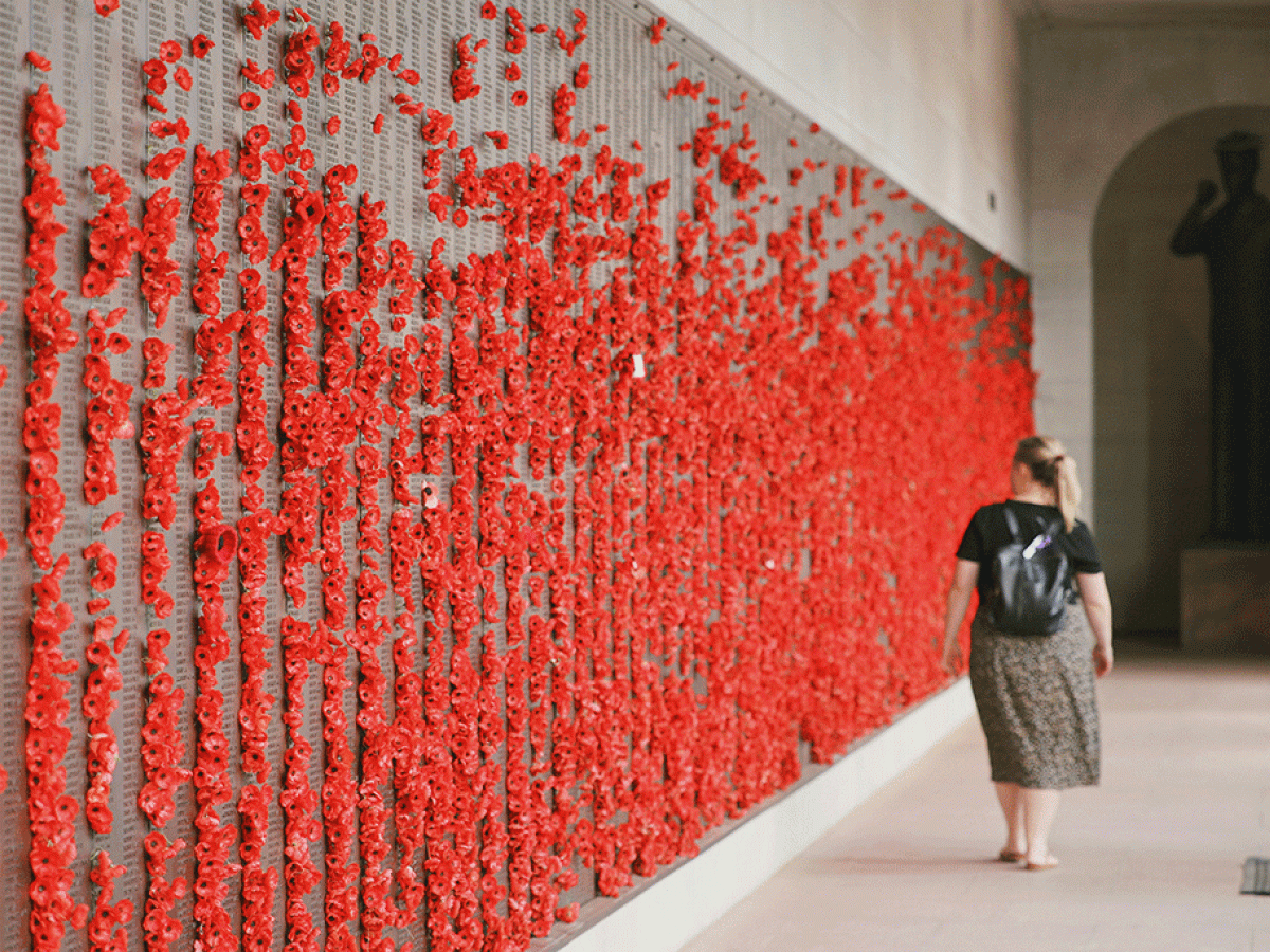 A woman walls along a war memorial wall covered in red poppies.