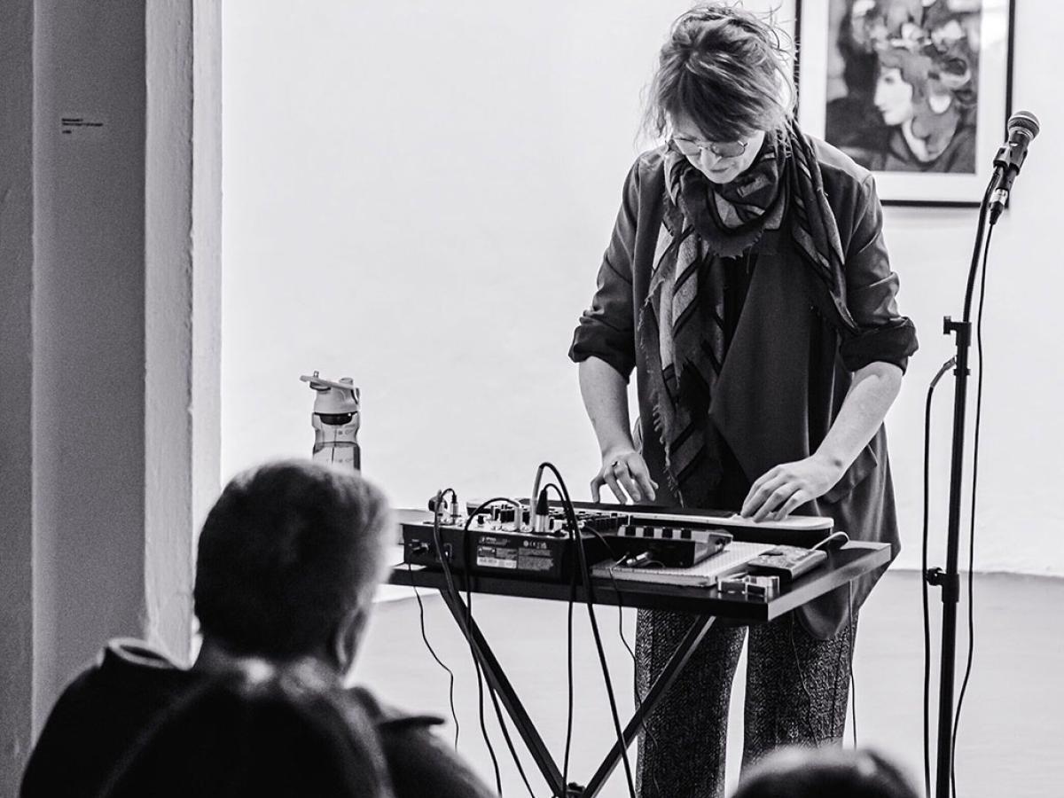 A woman stand at a mixing desk playing a small keyboard.