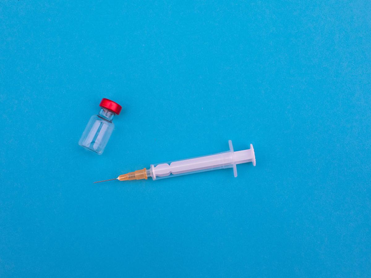 A vial and syringe lie on a blue backdrop.