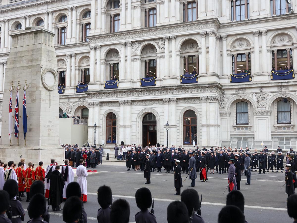 A Remembrance Sunday service stands to attention around a cenotaph.