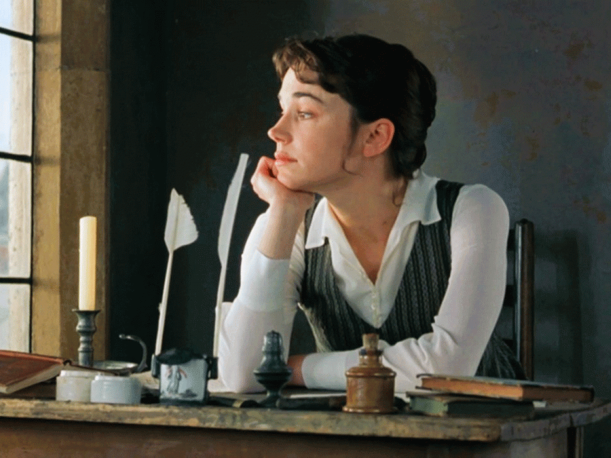 A 18th century woman sits at a desk, beside a candle and stares out the window.