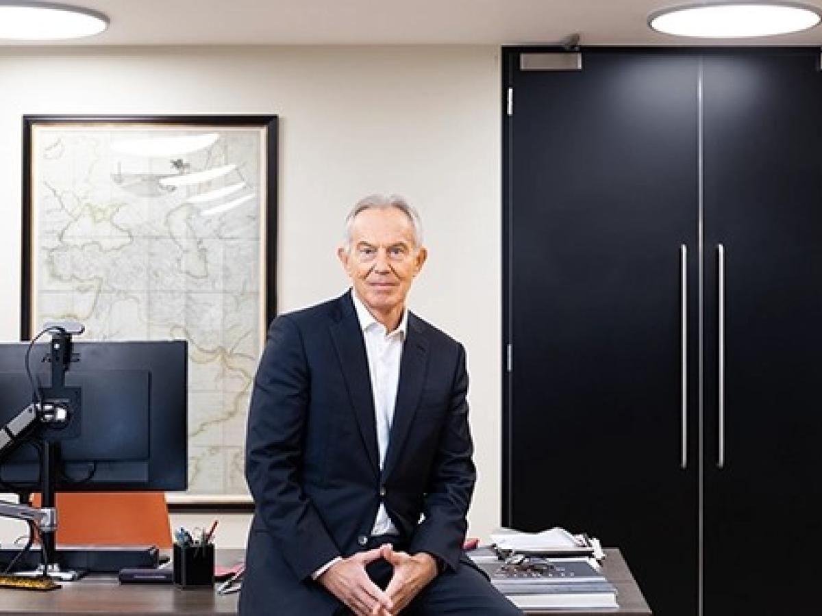 Tony Blair rests on the edge of a desk.