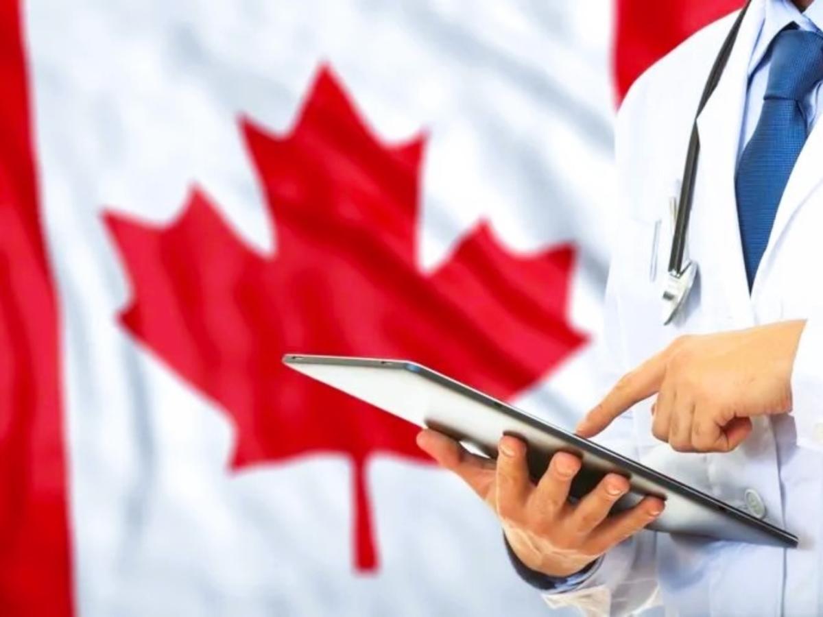 a doctor consults a tablet against the backdrop of a Canadian flag.