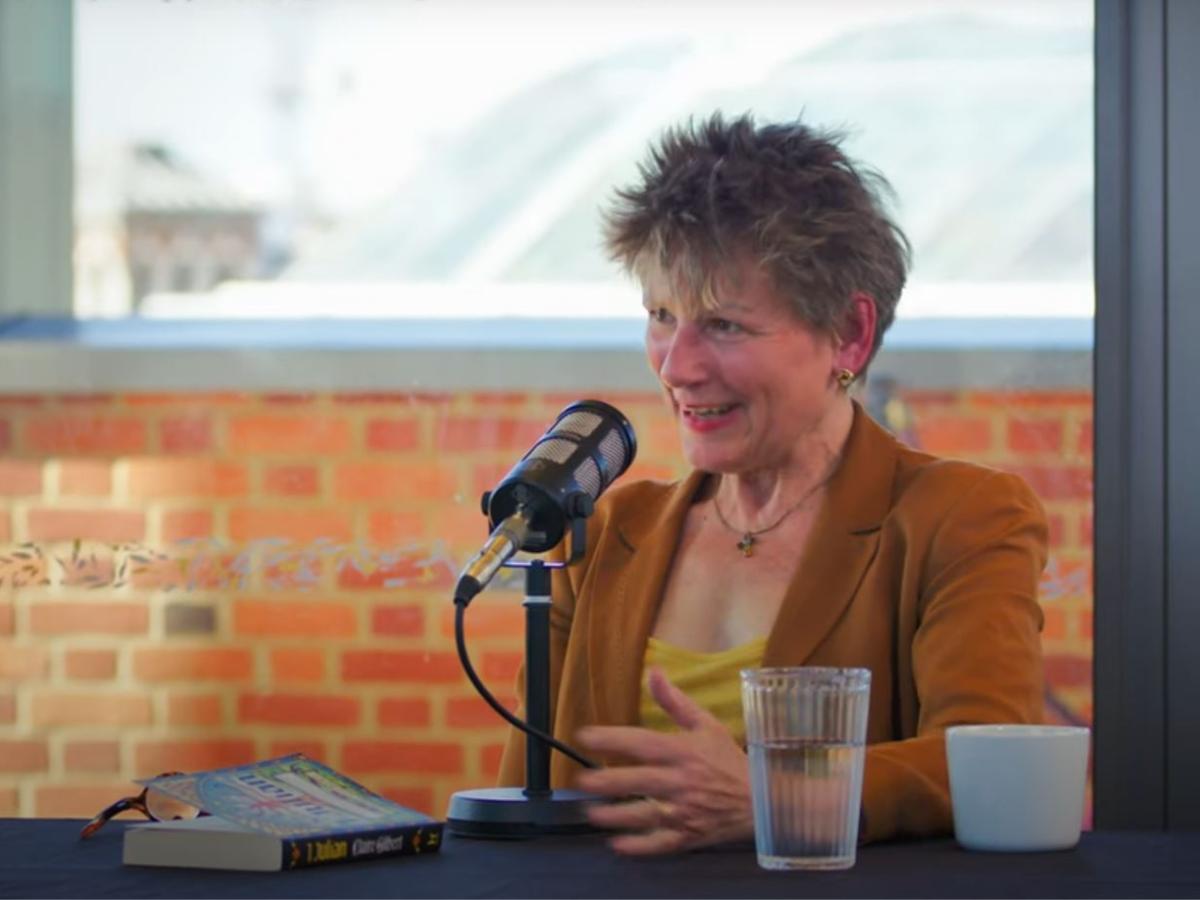 A woman sitting at a table in front of a microphone talks and gestures