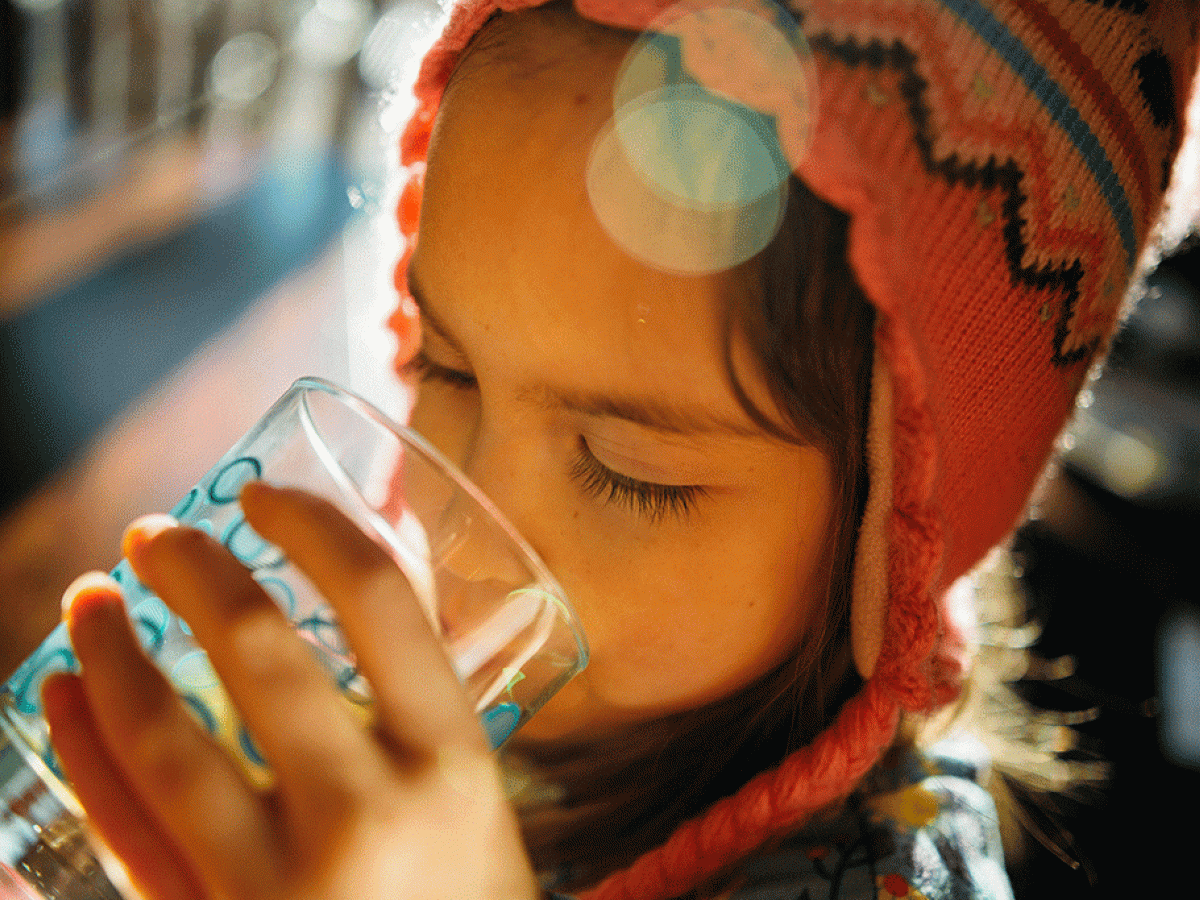 A child wearing a wool hat holds a glass and drink water from it.