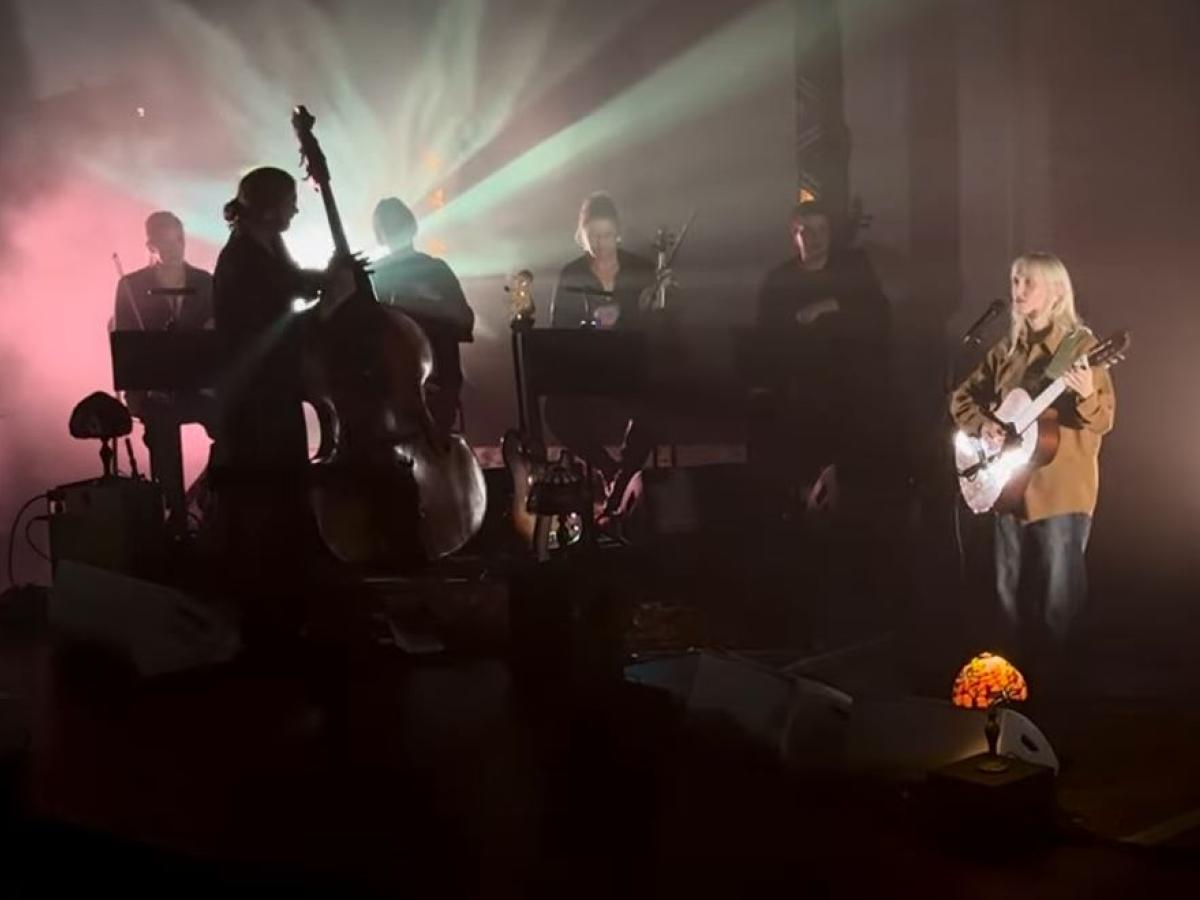 A misty back lit stage hosts a singing guitarist and a double base player