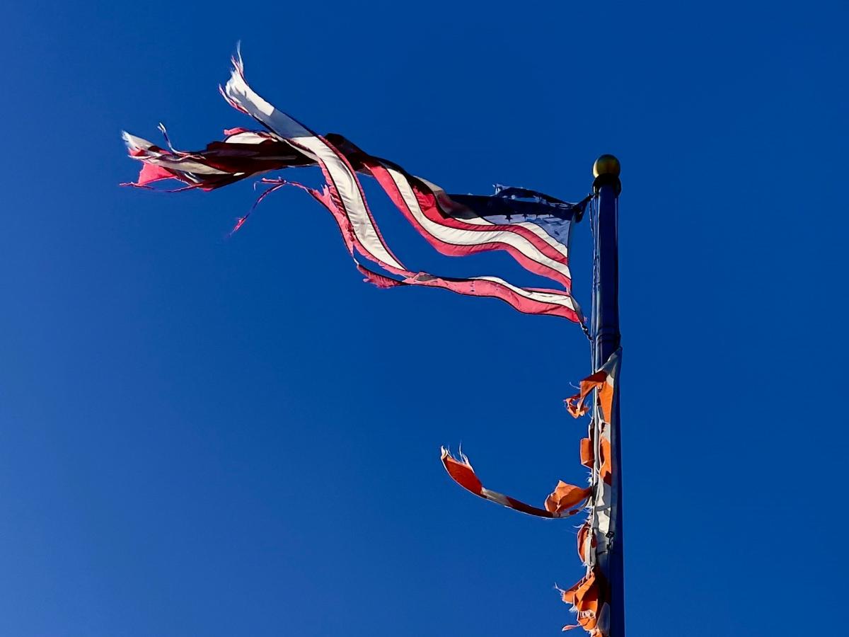 a tattered American flag flies against a blue sky.