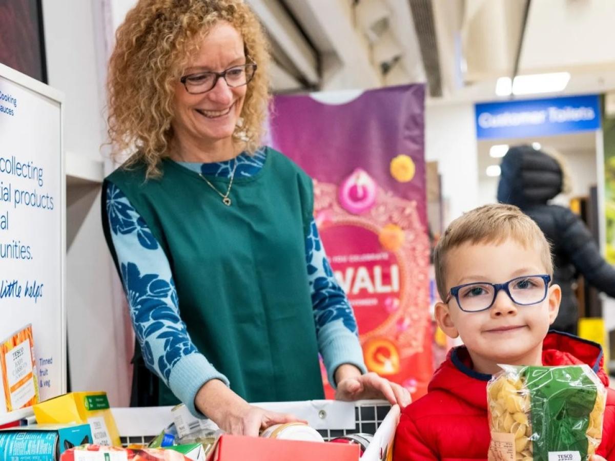 A shop assistant stands by a foobank trolley, while a child holds a packet of pasta beside it