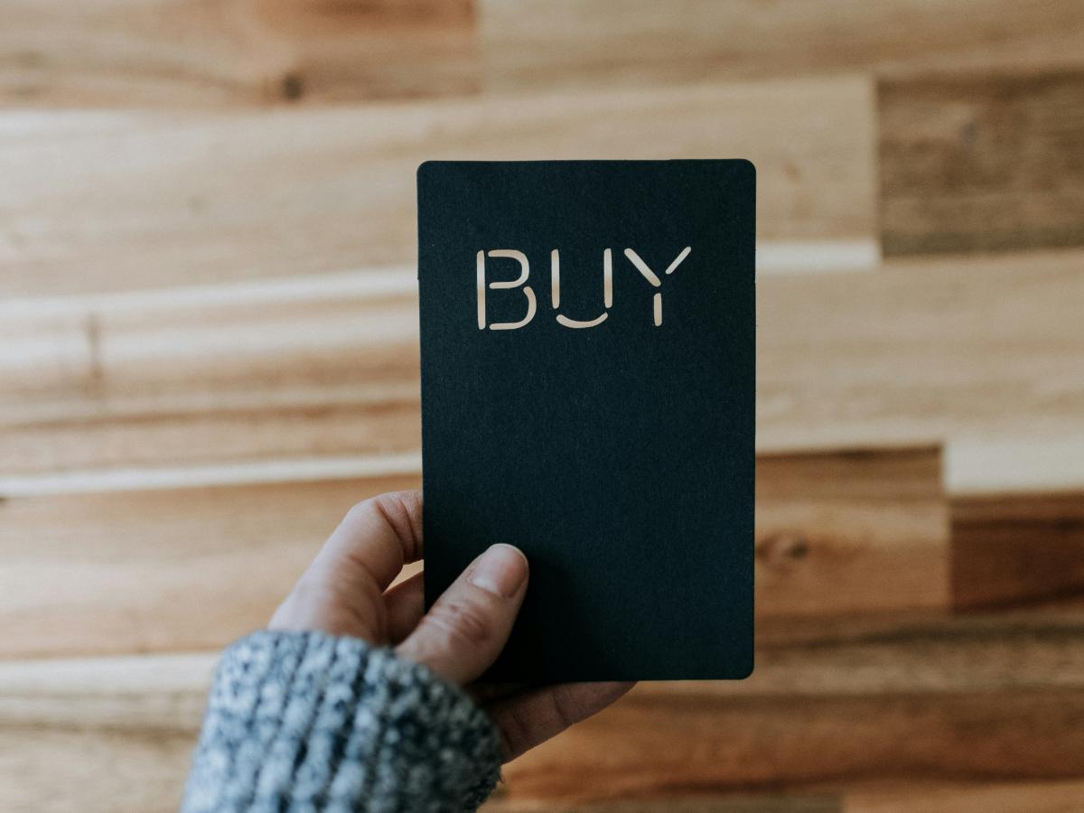 a hand hold a black payment card that reads 'buy'.