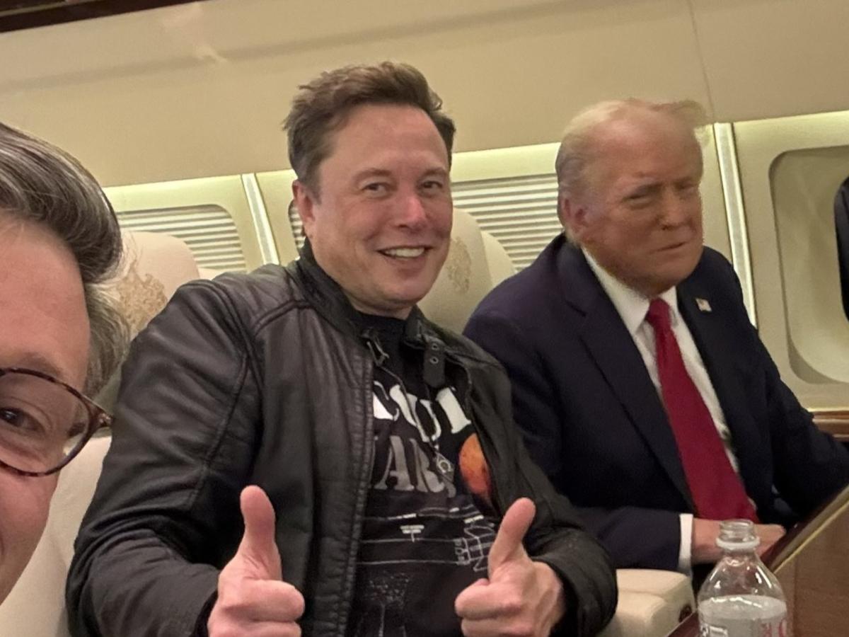 Elon Musk sits next to Donald Trump on a plan, while giving the thumbs up gesture with both hands.