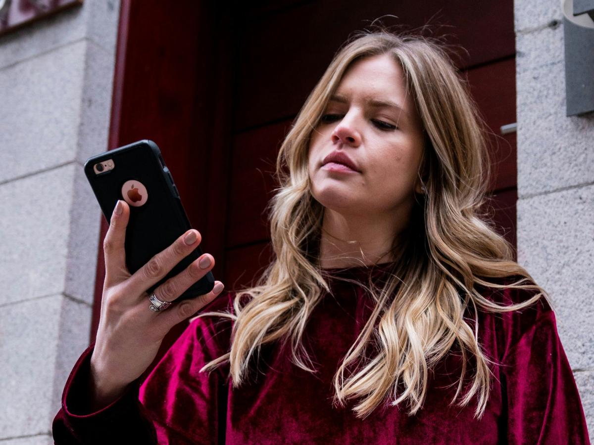 A woman holds her phone up in her hands and looks at it in a slightly vexed way.