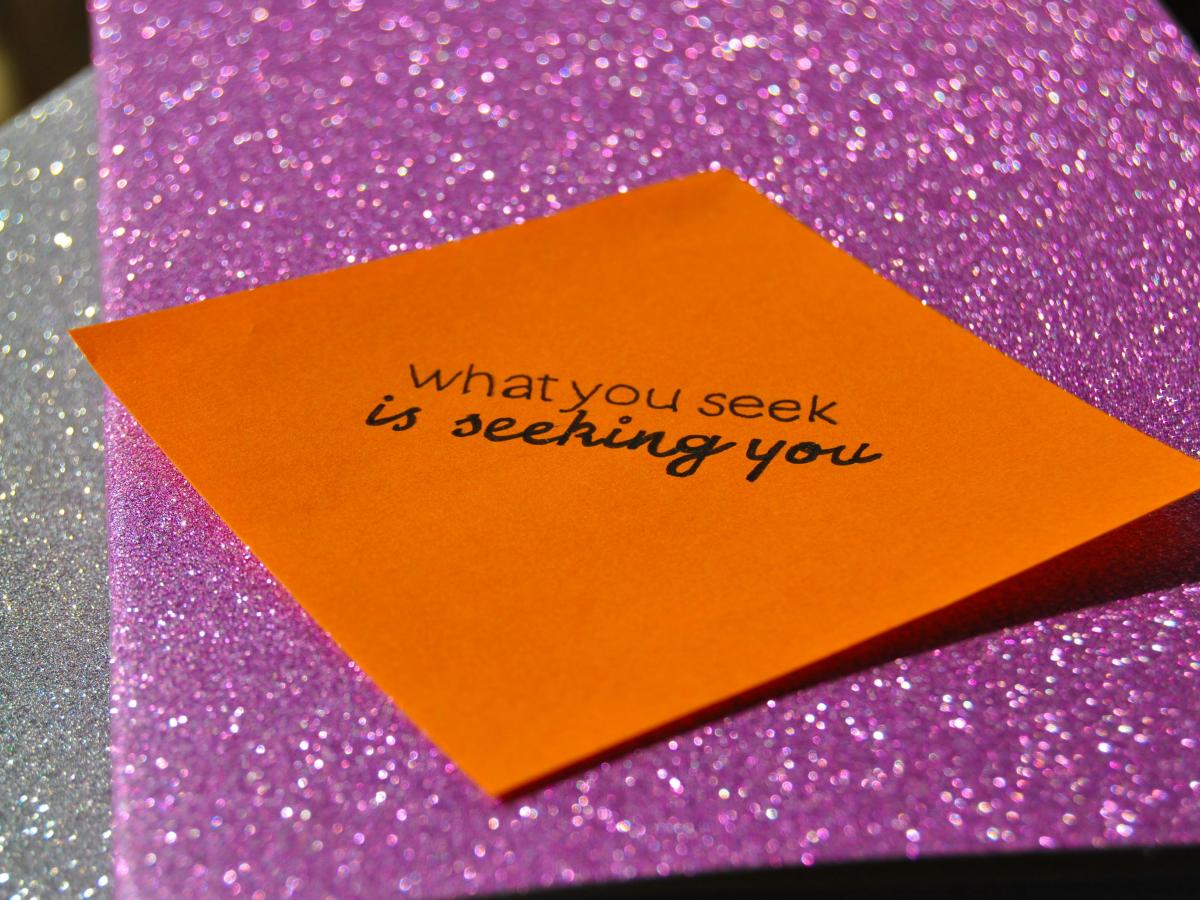 Against a purple glittery background, a orange notelet reads: 'what you seek is seeking you.'