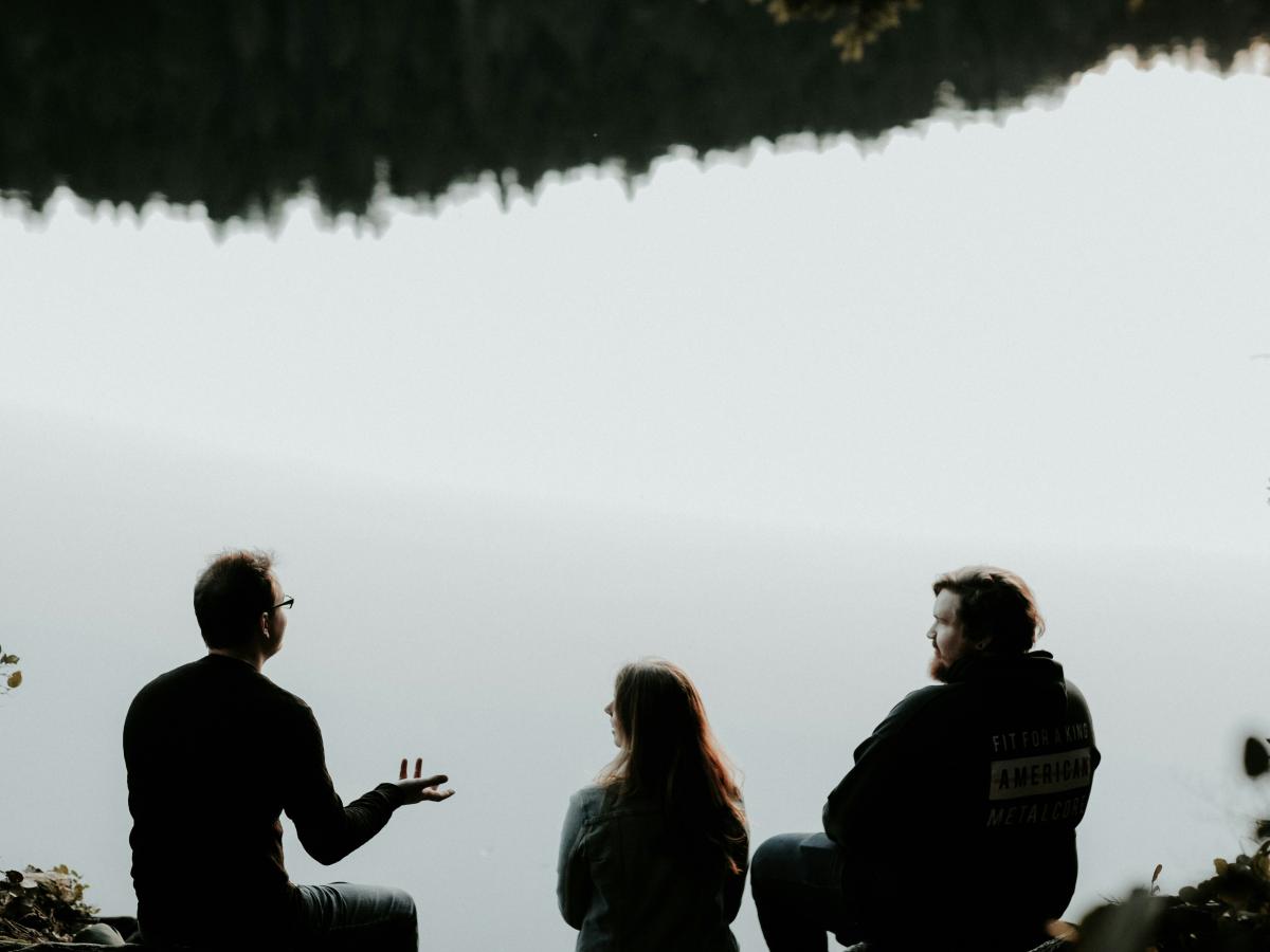 Three people sitting looking out over viewpoint are silhouetted against the sky. 